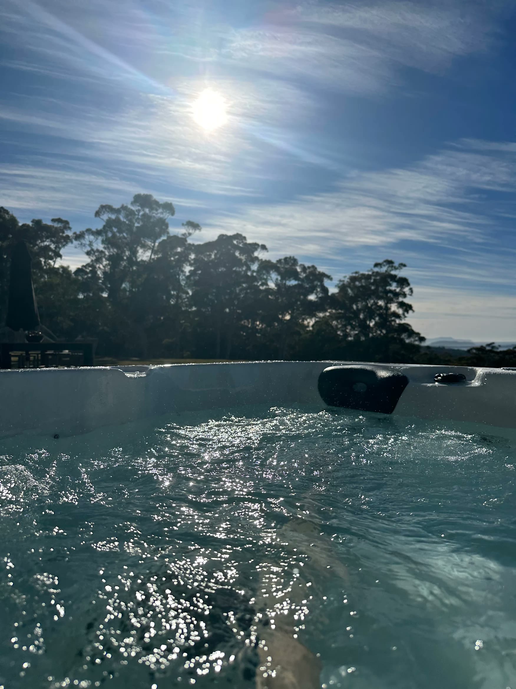 View from inside a spa over sunlit water to trees and sky