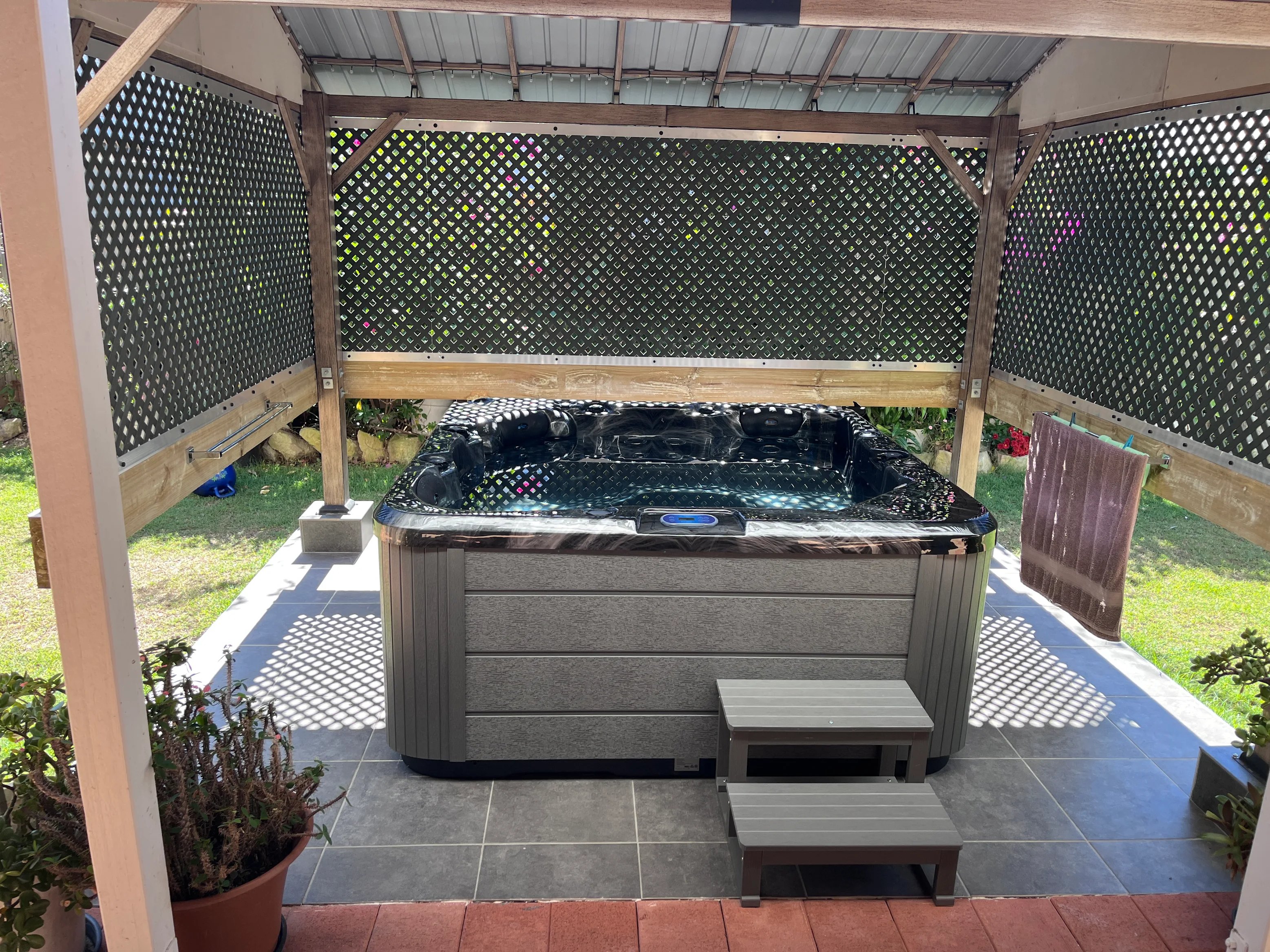Spa under a timber pergola with a lattice screen, beside a back lawn