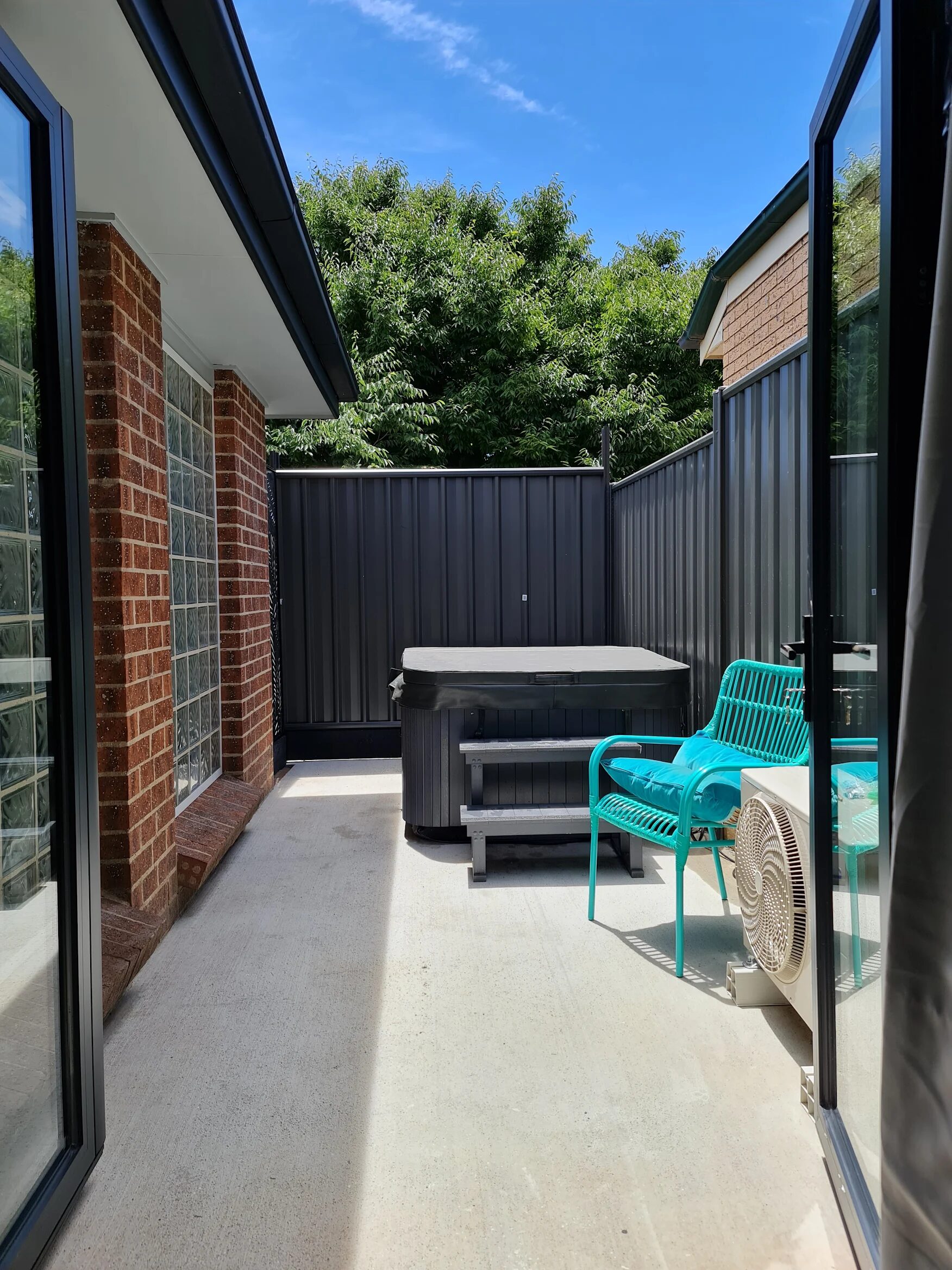 A spa with its cover on, installed in a narrow side courtyard between a house wall and a fence