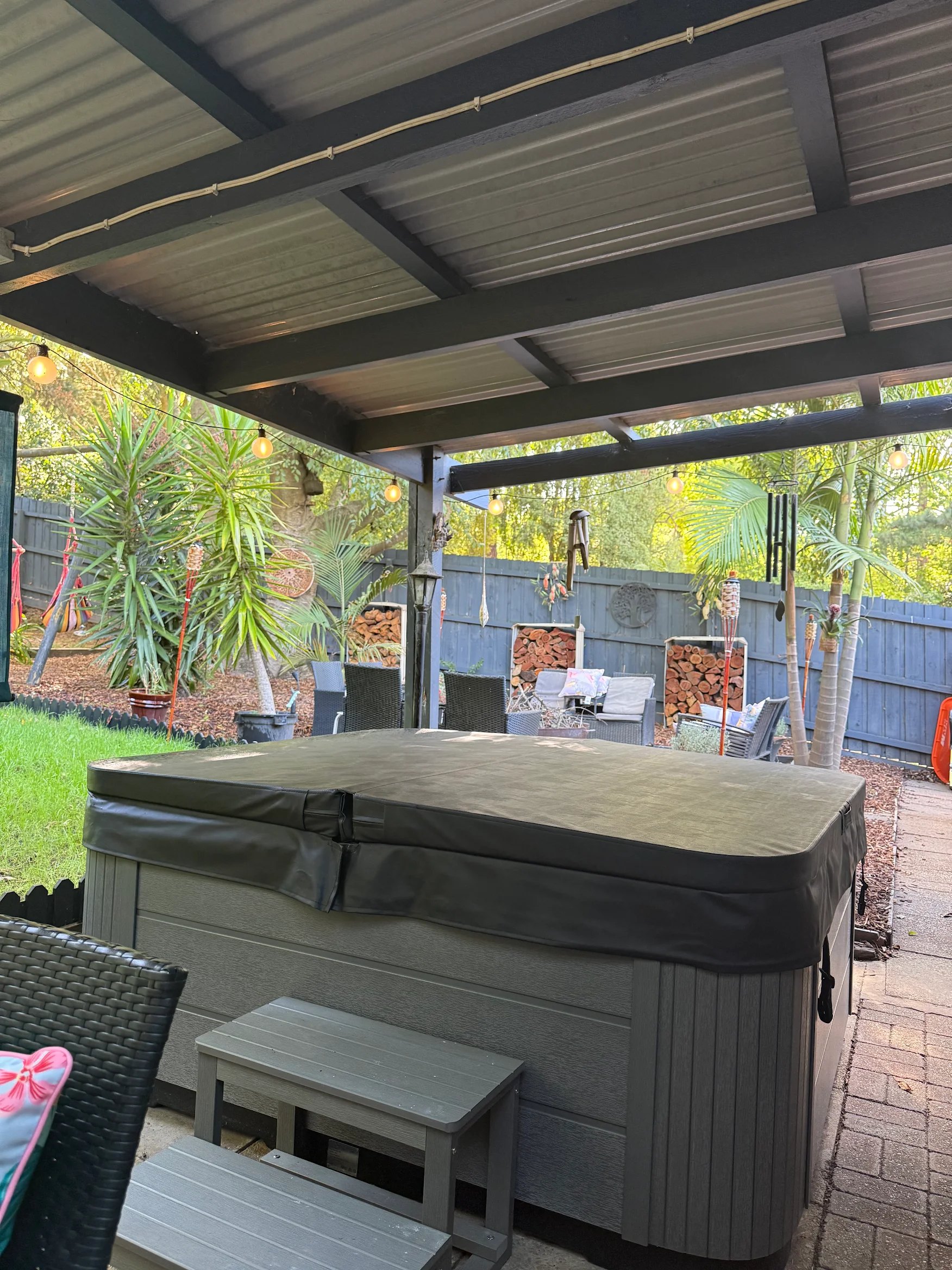 Spa under a backyard patio roof surrounded by garden plants