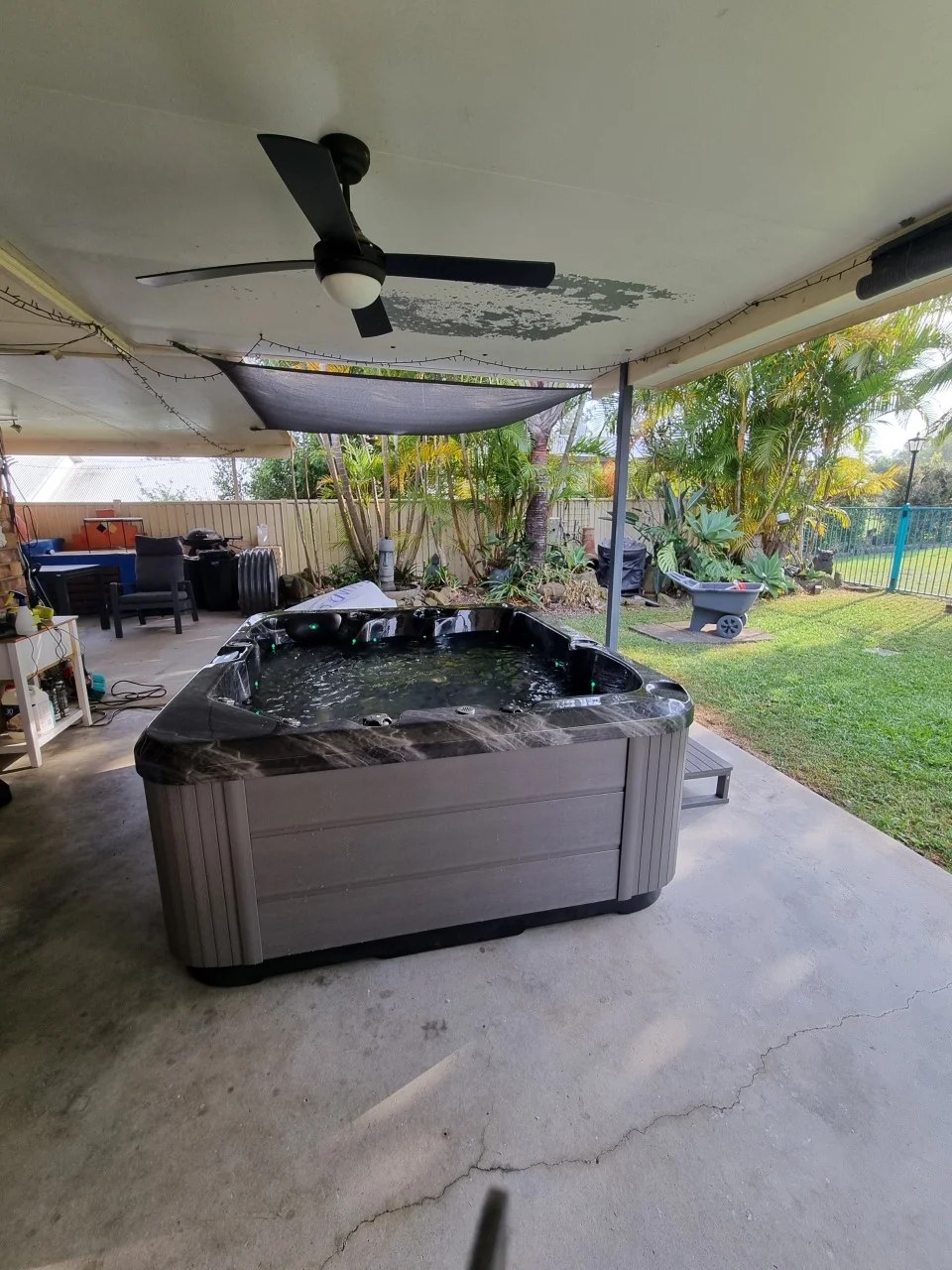 A spa filled and running under a backyard patio with a ceiling fan