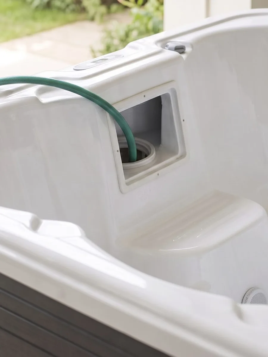 A garden hose running over the rim of an empty spa and down into the open filter box to fill it.