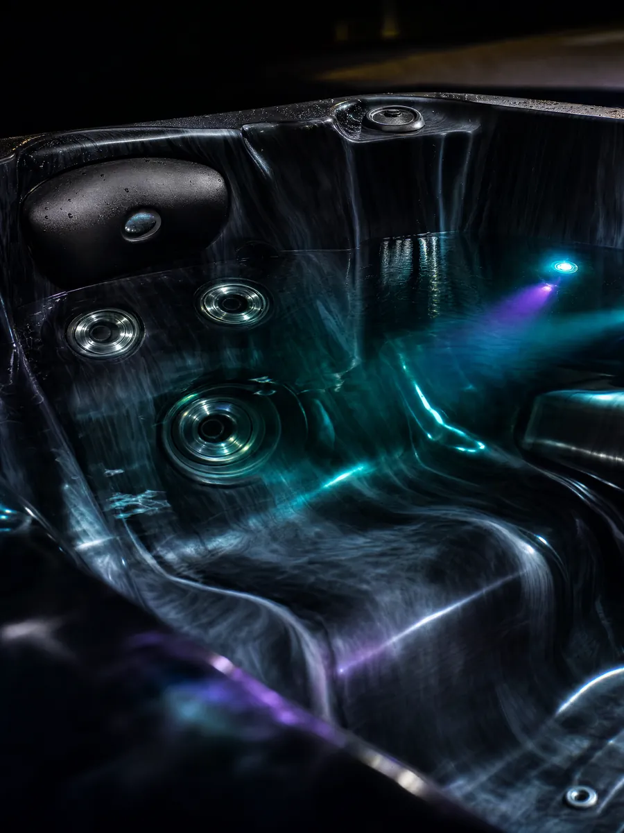 The spa interior at night with the multicoloured LED wall lights glowing teal and violet through the water.
